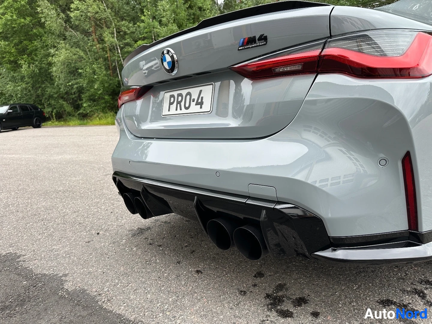 White BMW coupe rear detail showing red tail light, dual exhaust pipes, and M badge on trunk