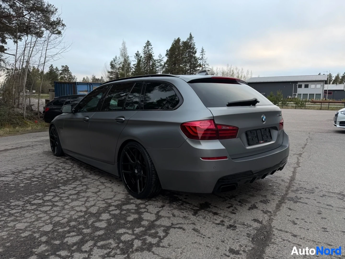 Harmaa BMW farmari sivusta takaapäin kuvattuna pysäköintialueella