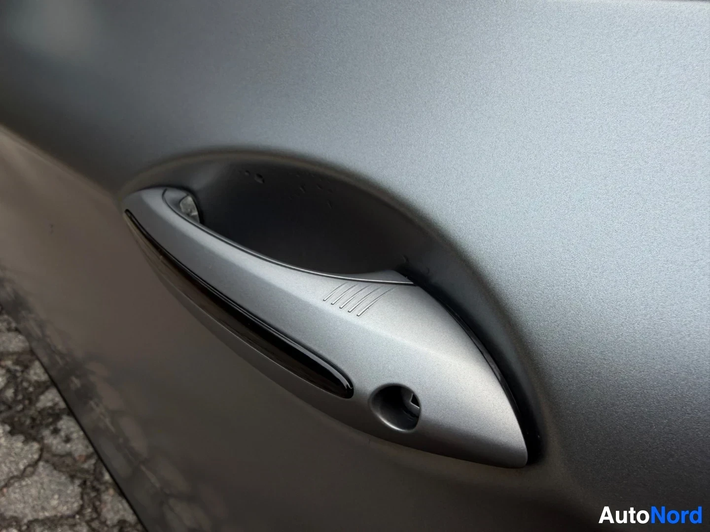 Silver door handle with lines detail on gray vehicle side
