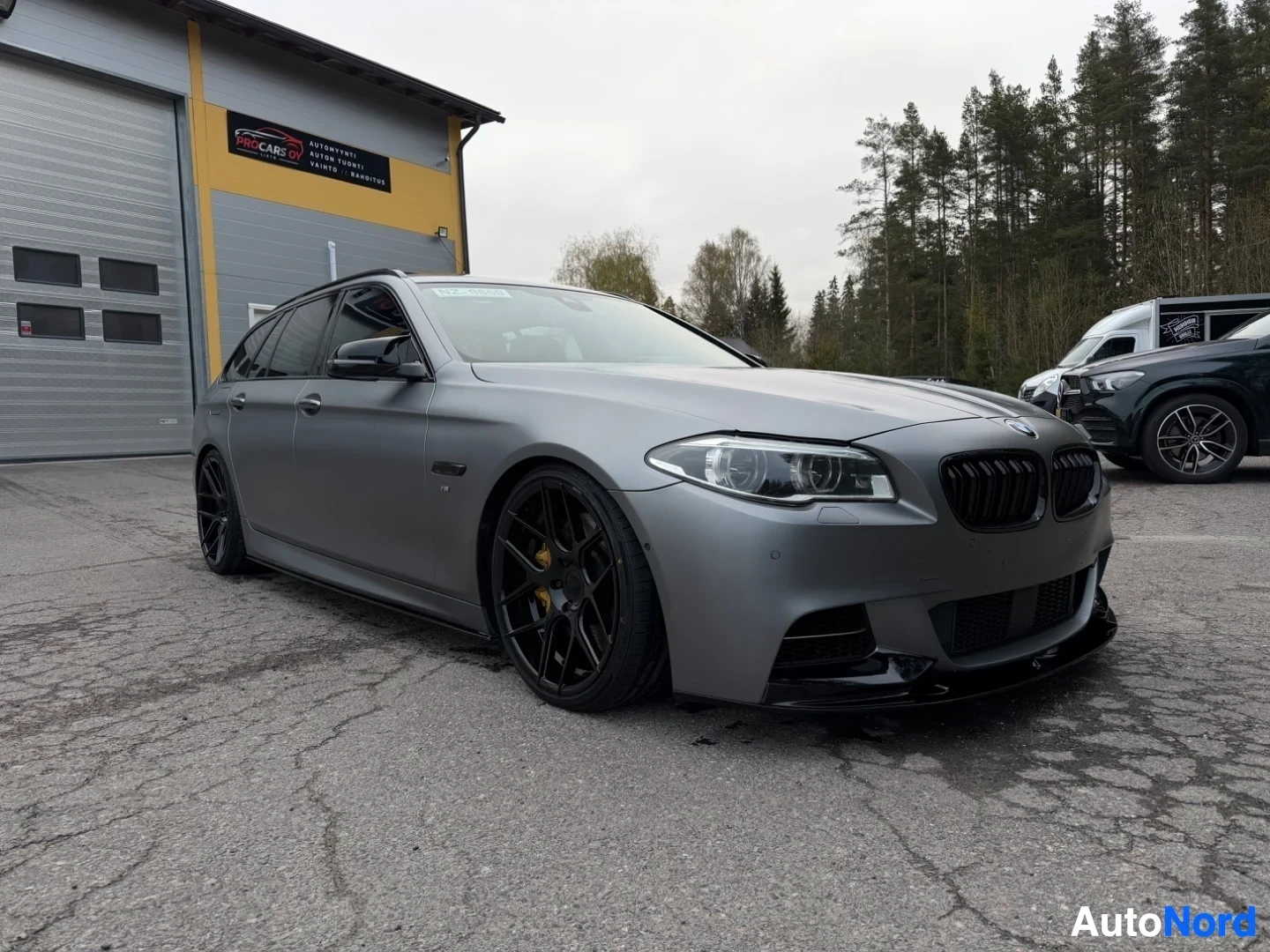 Harmaa BMW farmari näkyy sivusta vasemmalta puolelta varikolla
