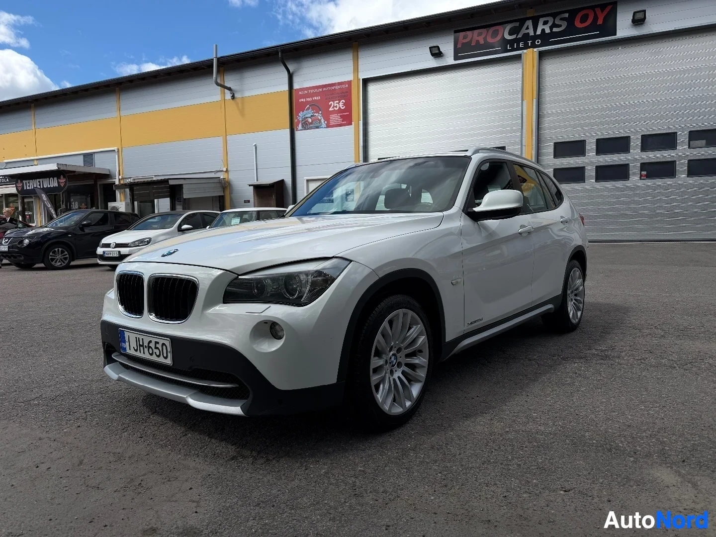 White BMW X1 front left quarter view at dealership location with other vehicles nearby
