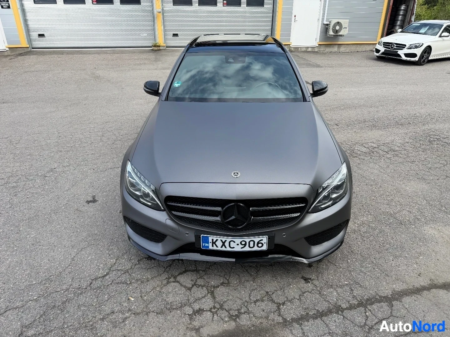 Mercedes-Benz farmari harmaa, suoraan edestä kuvattuna pysäköintialueella