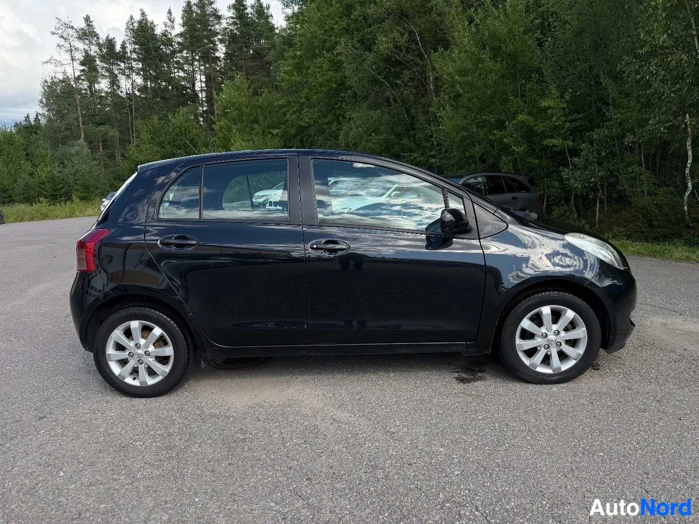 Black Toyota Yaris profile side view with forest background