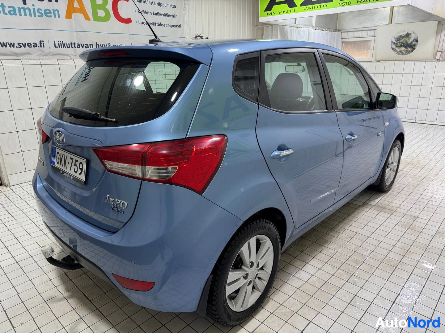 Takaviisto: Sininen Hyundai ix20 takaa ja vasemmalta viistosti kuvattuna. Autossa on alumiinivanteet ja talvirenkaat. Rekisterikilvessä. Autossa on peräkoukku.