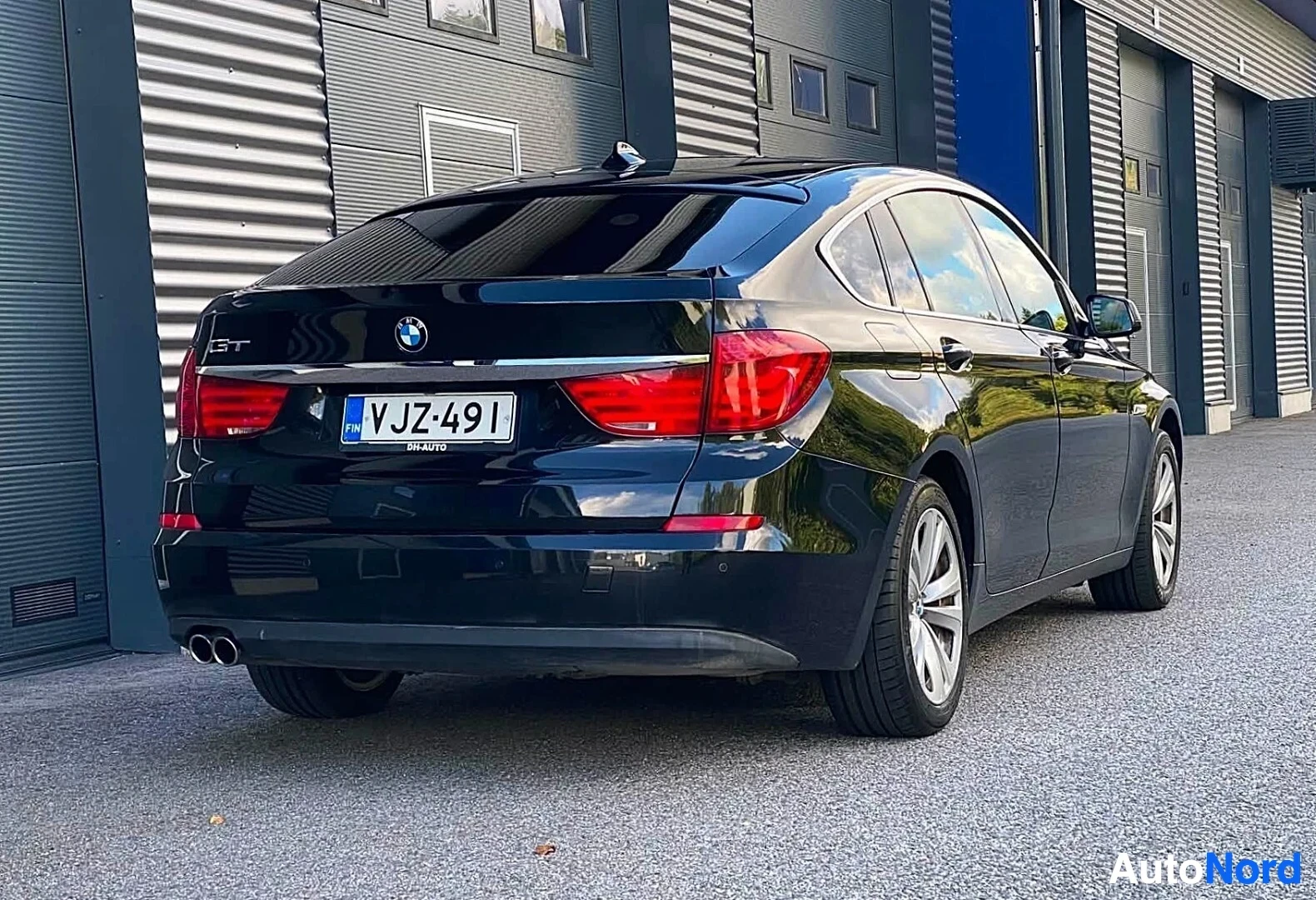 Takaviisto: Tummansininen BMW sedan kuvattu takaa ja oikealta puolelta, näkyvät takaa ja oikea sivu, rekisterikilvessä, tekstissä GT ja BM AUTO, kaksi pakoputkea nä