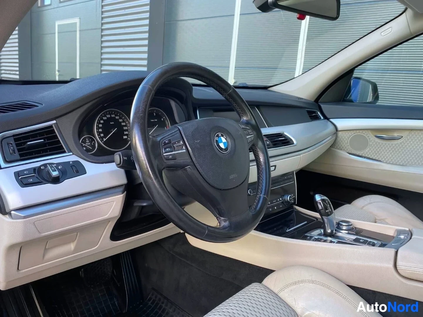 Ohjaamo: BMW:n ohjaamo vasemmalta puolelta kuvattuna. Näkyvissä on musta monitoimiohjain, kahden mittarin instrumentti, vaaleat nahkaverhoillut istuimet ja keskikonsoli.
