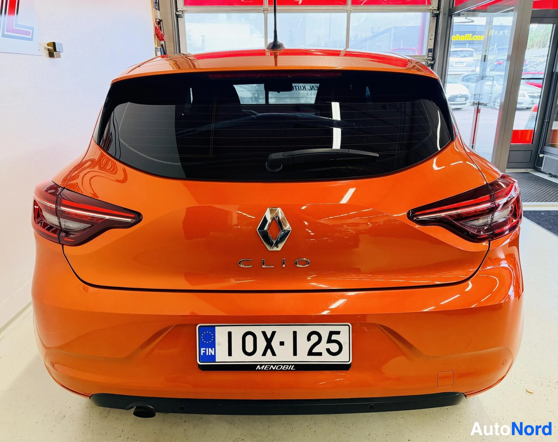 Takaa: Oranssi Renault Clio takaa kuvattu. Näkyvät takalamppu, rekisterikilpi '' ja Clio-merkintö