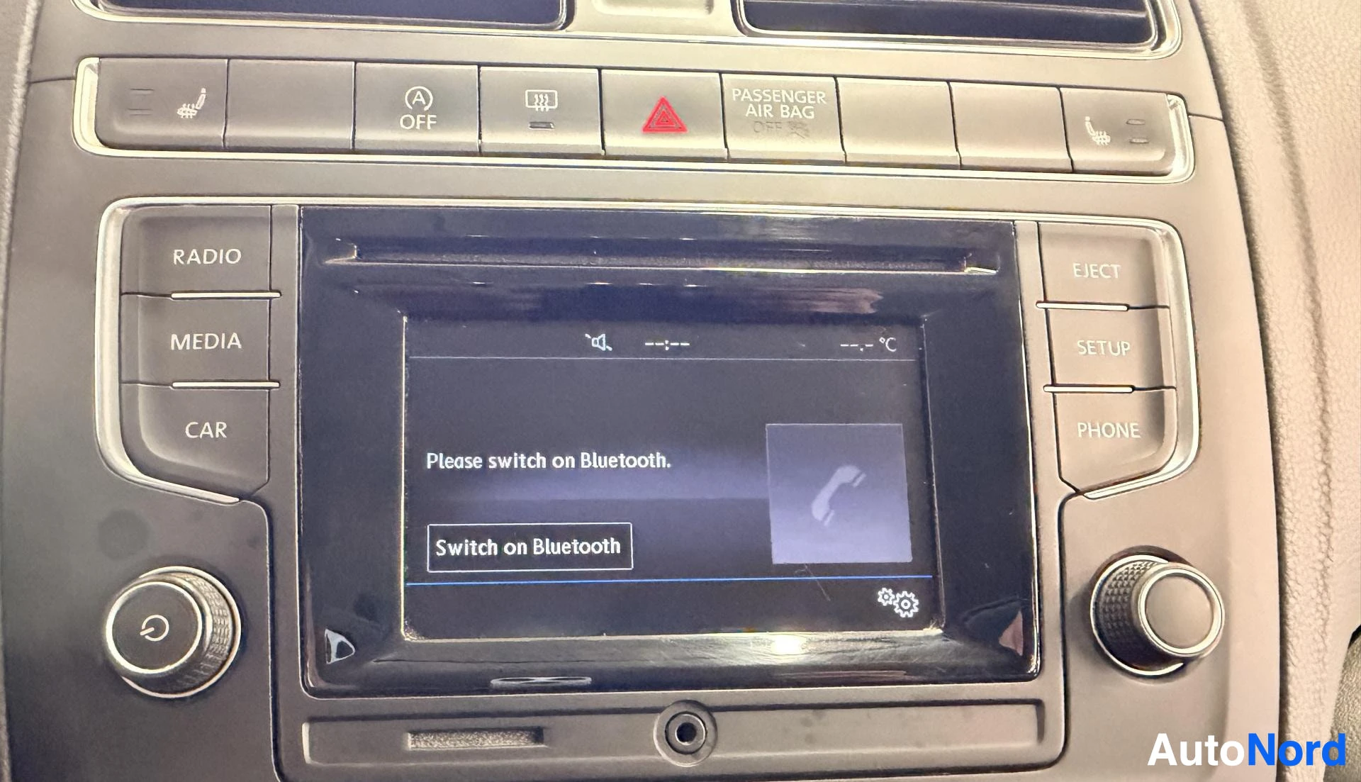 Yksityiskohta: Auton keskikonsolin infotainment-näyttö. Näytöllä näkyy viesti 'Please switch on Bluetooth.' ja nappi 'Switch on Bluetooth'. Ylhäällä näkyvät hallintapainikkeet