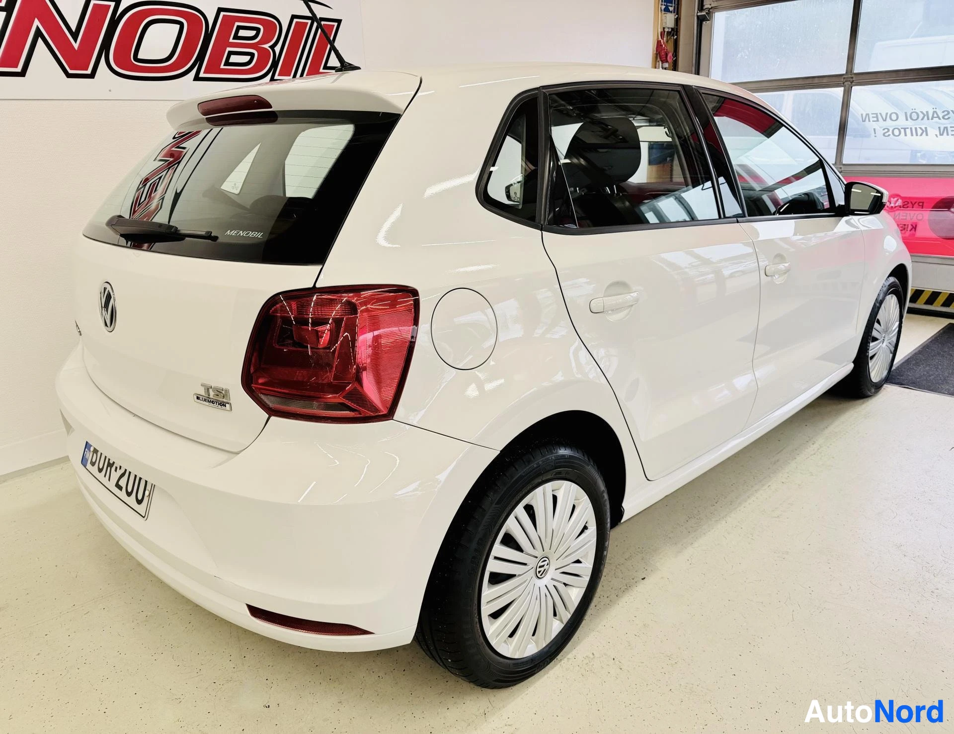 Takaviisto: Valkoinen Volkswagen Polo kolme neljäsosaa takaa oikealle, punainen takavalo, valkoinen vanne, sisätiloissa, ovi auki