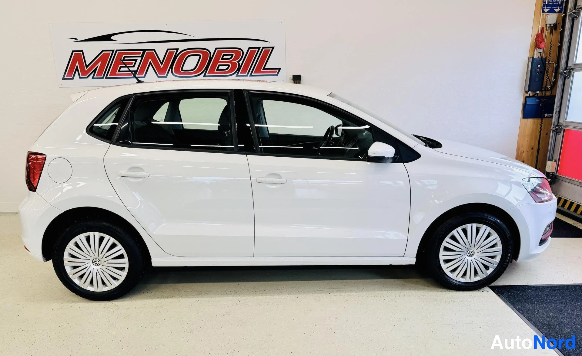 Sivulta: Valkoinen Volkswagen Polo sivusta vasemmalle, valkoinen vanne, mustien ikkunoiden kehykset, sisätiloissa showroom-nopeutena