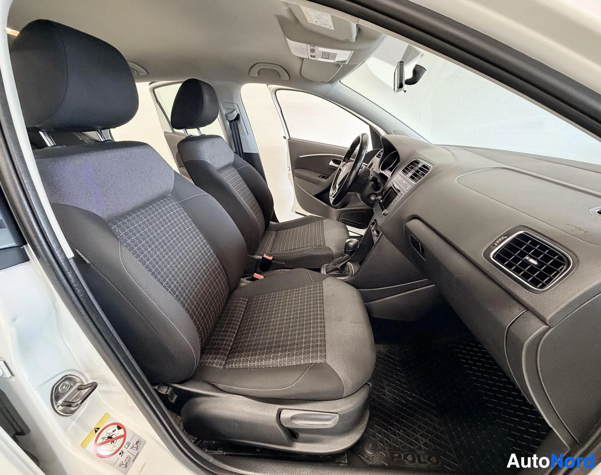 Etuistuimet: Volkswagen-auton etupenkki sisältä kuvattuna kulmasta. Harmaat kangaspäälliset istuimet, mustavalkoinen ohjauspyörä, beige sisustus. Lattiamatot näkyvissä.