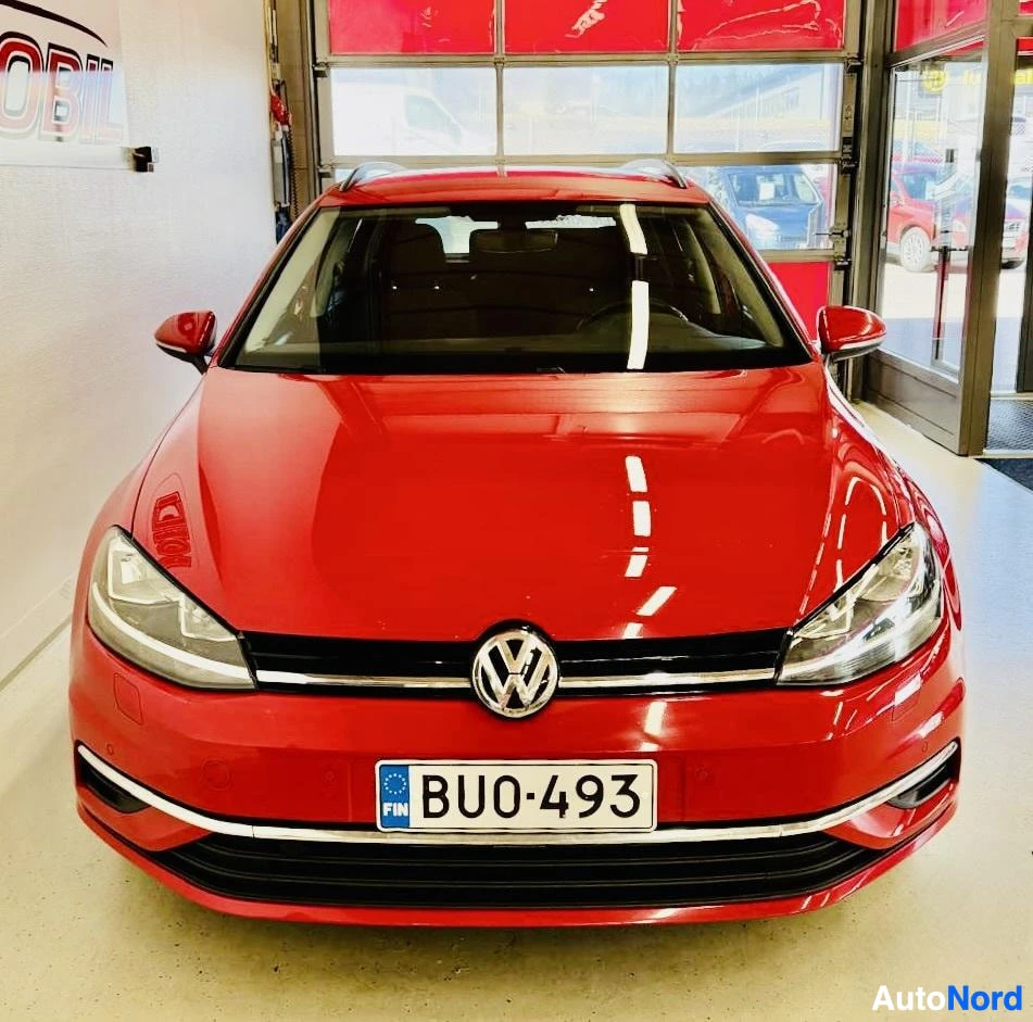 Edestä: Punainen Volkswagen Golf, etunäkymä suoraan. LED-ajovalot, Volkswagen-tunnus keskellä grillissä. Rekisterinumero näkyy etuosassa. Punainen peili vasemma