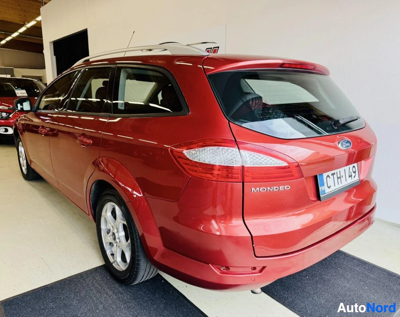 Takaviisto: Punainen Ford Mondeo farmari kuvattu takakolmesta neljäsosasta. Takapuoli ja vasen sivu näkyvät. Rekisterikilpi näkyy selvästi. Takaikkunassa on harmaa