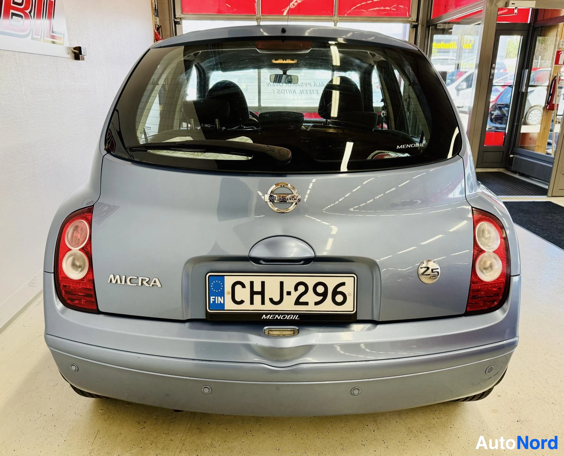 Takaa: Nissan Micra takaosa, hopea väri, rekisterikilvessä CHJ296, näkyy MICRA-teksti, 25-merkintä, punainen takavalo, tumma lasit, sisätila näkyvissä.