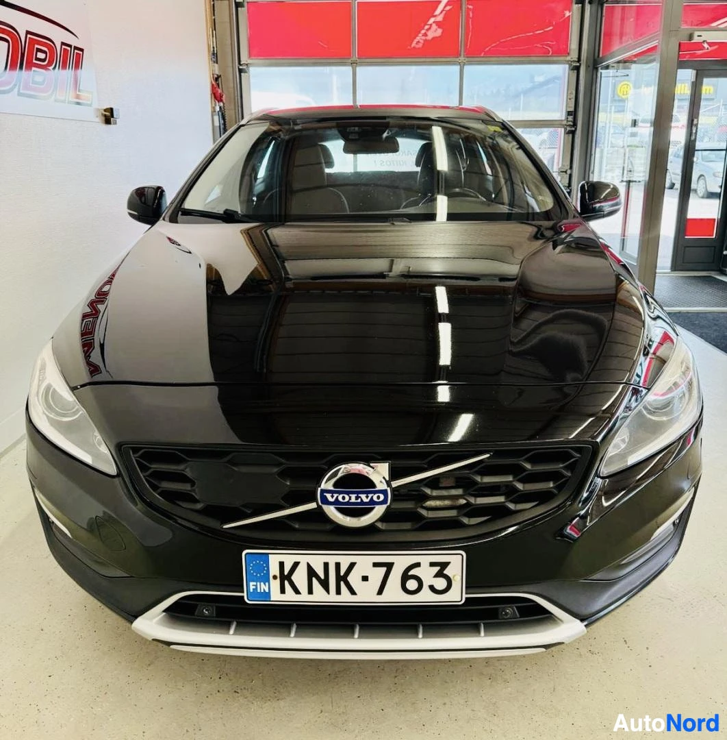 Edestä: Musta Volvo V60 näkymässä edestä. Rekisterikilpi näkyy. Volvo-logo näkyy grillissä. Valkoinen kromi-liina alla