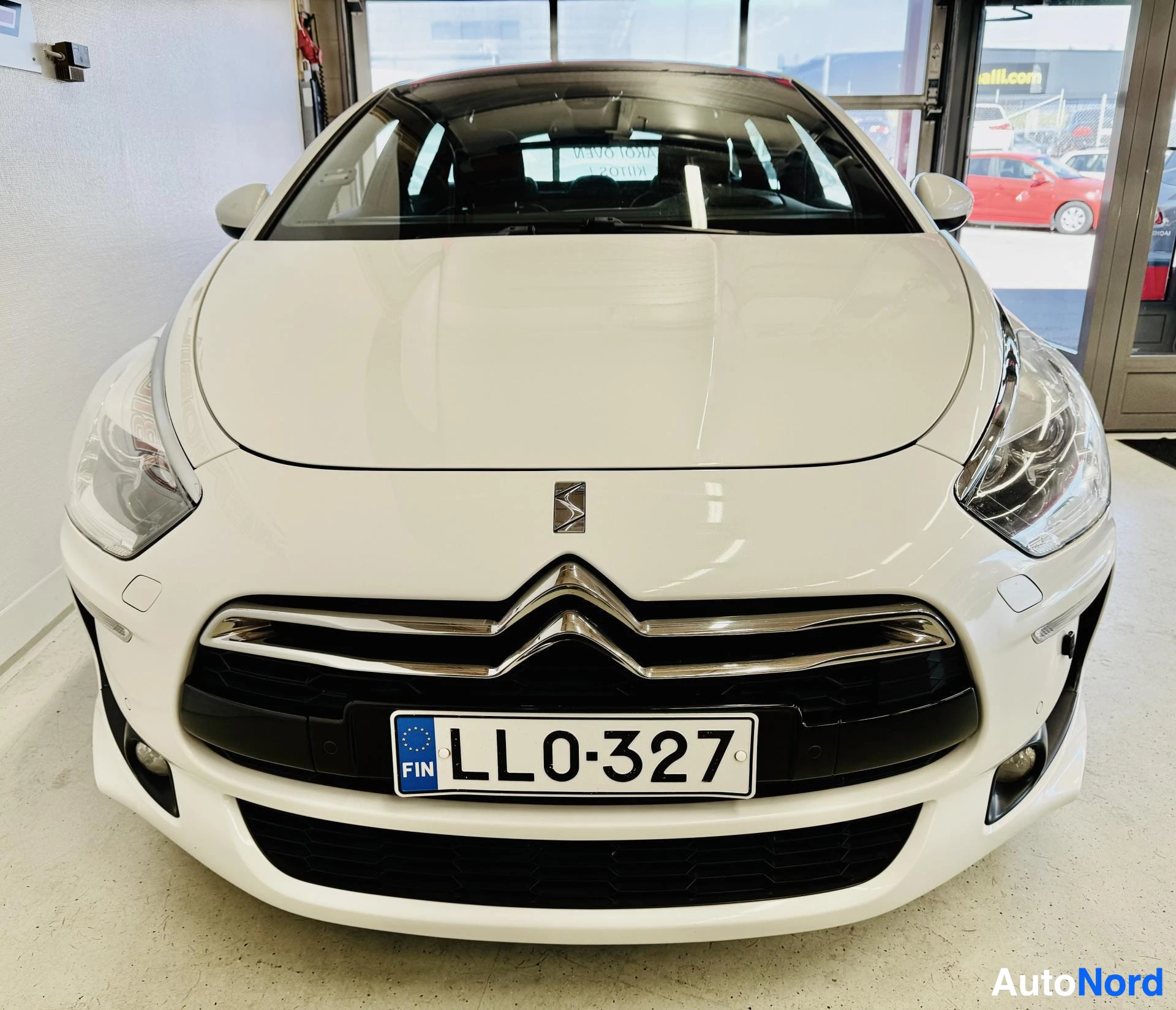 Edestä: Valkoinen Citroën-auto näkyy edestä. Näkyvät LED-päivävalojen hohtavat renkaat, kromi-viimeistelyinen grilli ja rekisterikylpi LL0327.