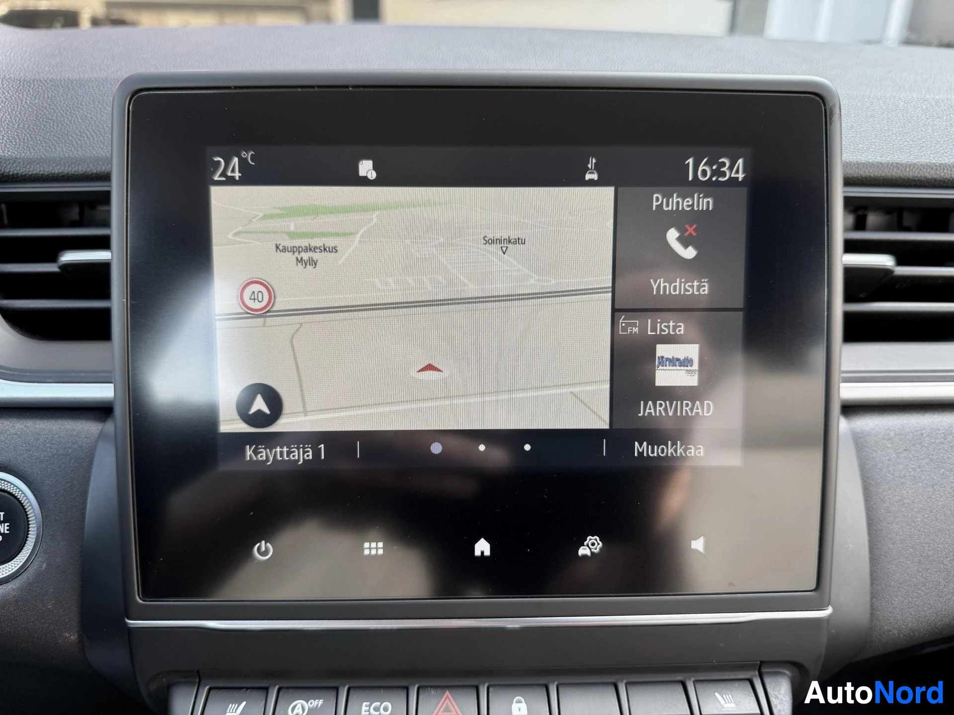 Yksityiskohta: Auton infotainment-näyttö näyttää navigointikarttaa ja kellonaikaa 16:34, sisälämpötila 24°C, puhelin yhdistetty