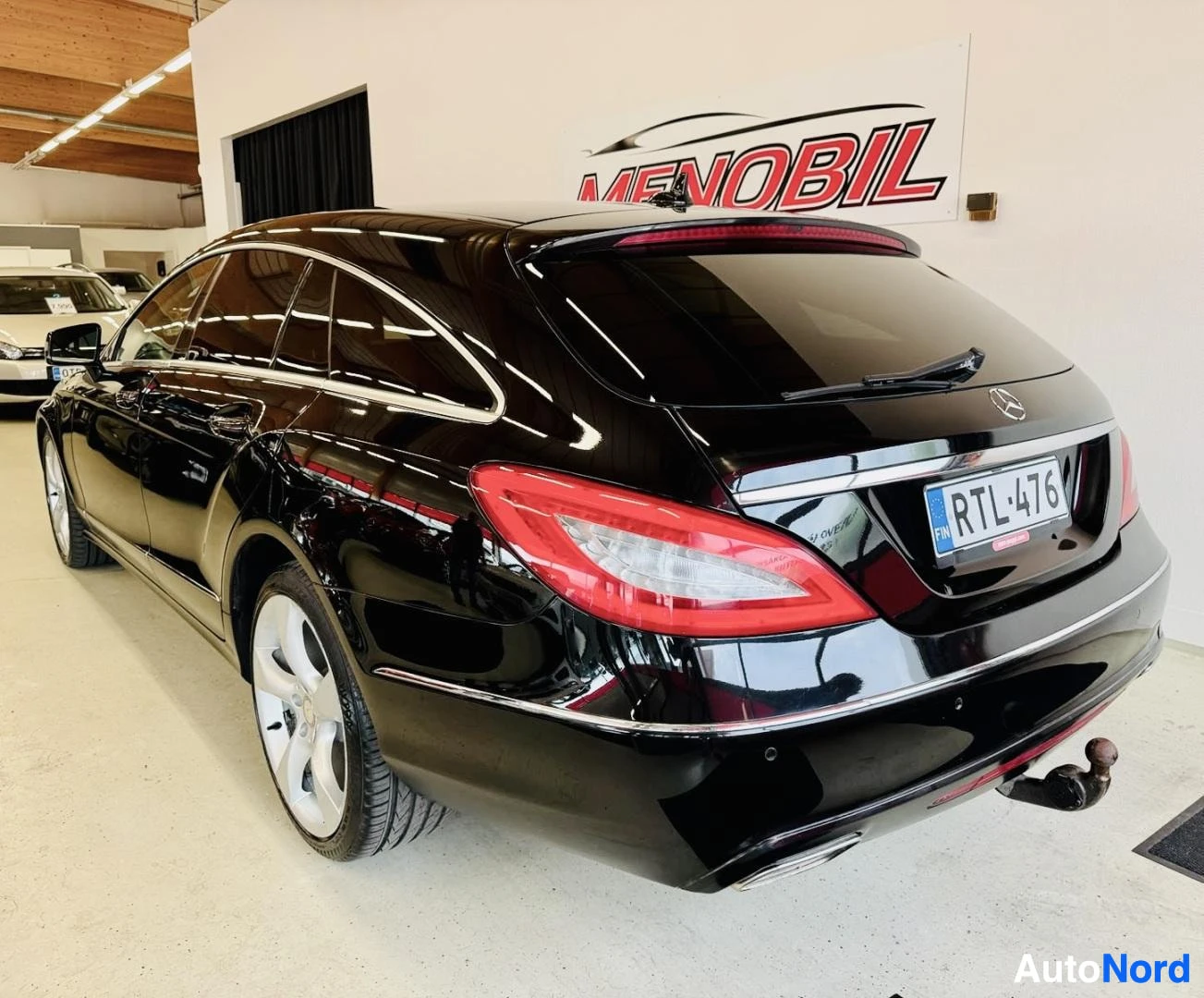 Takaviisto: Musta Mercedes-Benz CLS Shooting Brake takapuolelta oikealta, punaiset takavalaisimet, RTL-rekisterikilpi, vetokoukku näkyvissä, hallissa
