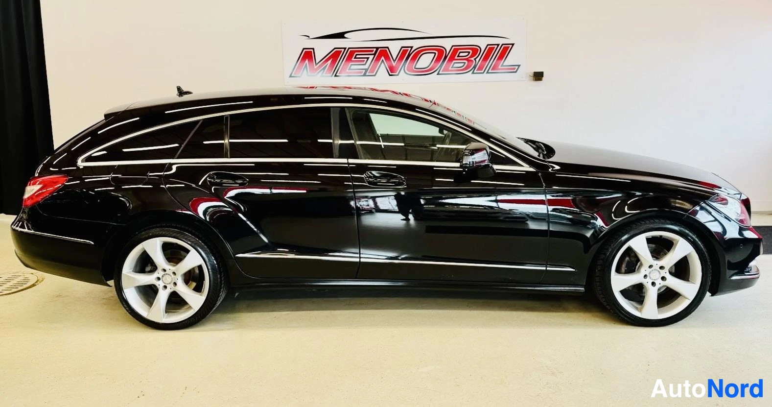 Sivulta: Musta Mercedes-Benz CLS viistoperä profiilista vasemmalta, valkoväliset renkaapyörät, sisätiloissa halogeenivalaistus