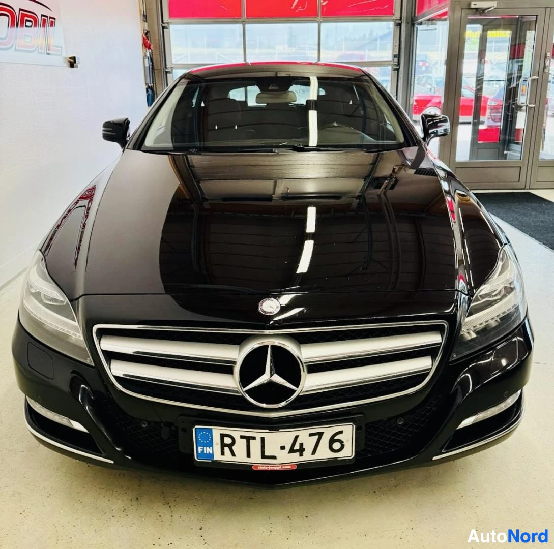 Edestä: Musta Mercedes-Benz CLS etumerkki, etulasi avoin, kolmikulmainen Mercedeksen tunnus etuosassa, rekisterinumero näkyvissä