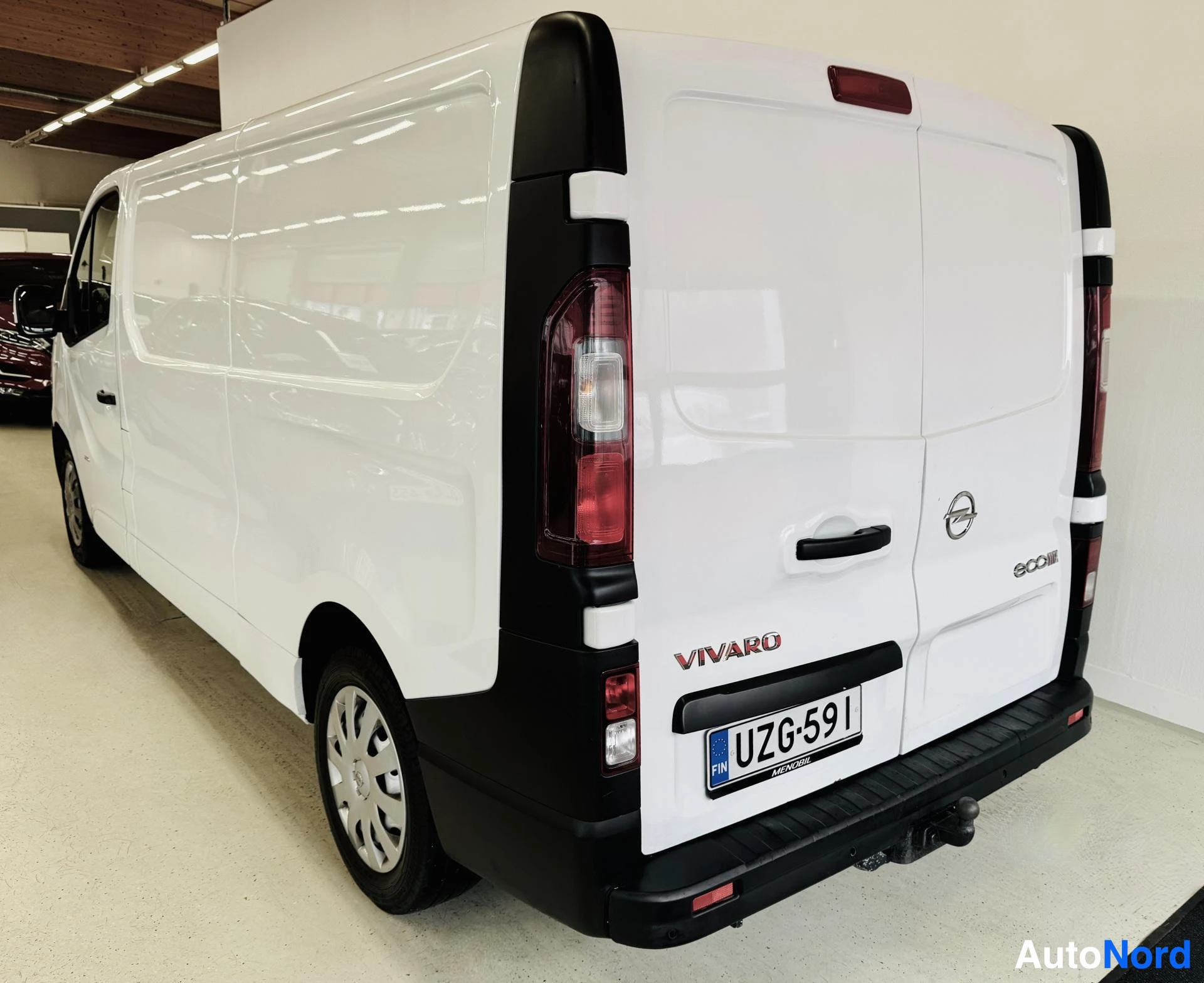 Takaa: Valkoinen Opel Vivaro -pakettiauto takanäkymässä, UZ6C591 rekisterikilpi ja VIVARO-teksti näkyvissä, tow bar asennettu, hallissa
