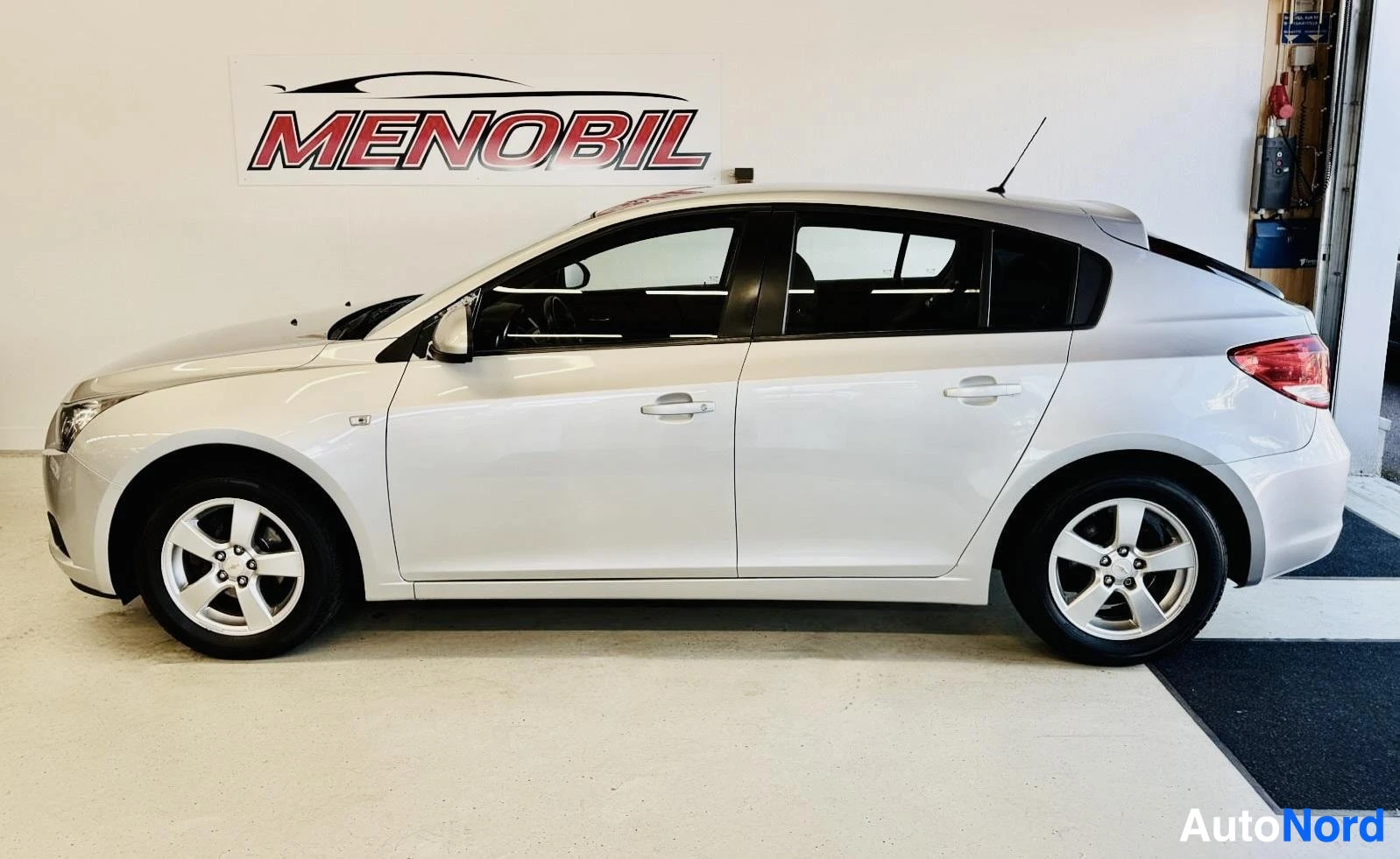 Sivulta: Valkoinen Chevrolet Cruze, sivusta katsottuna vasemmalta oikealle. Neljä ovea auki, kultalanganväriset vanteet, mustilla väreillä aksentoidut sivupintakehykset.