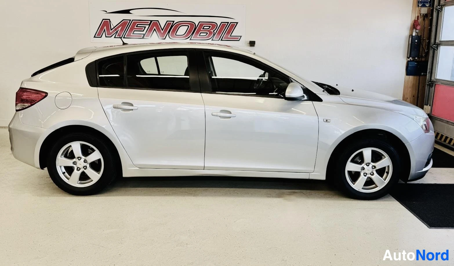 Sivulta: Valkoinen Chevrolet-hatchback sivukulmasta oikealle, vaalealla hallialustalla, valkoiset vanteet, musta katto