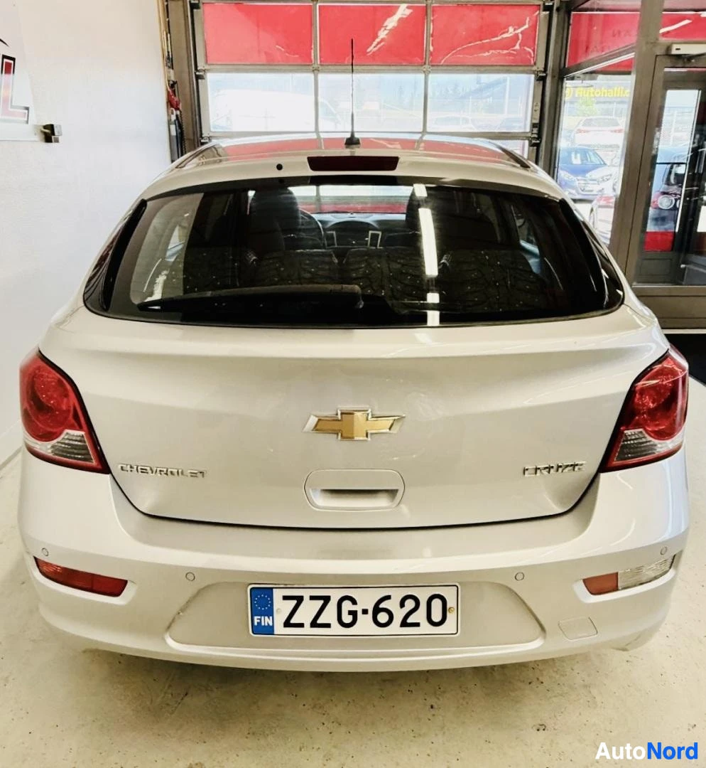 Takaa: Valkoinen Chevrolet Cruze takaapäin hallissa, rekisterikilpi FIN, punaiset takavalaisimet, musta katto