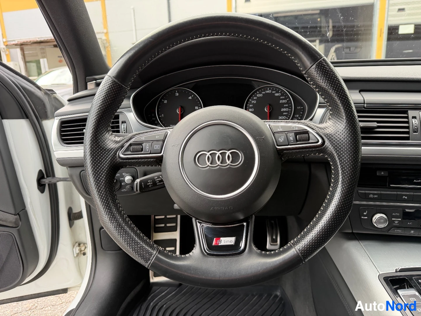 Yksityiskohta: Lähikuva auton ohjauspyörästä ja mittaristosta. Ohjauspyörässä on Audi-logo keskellä ja monitoiminäppäimet. Mittaristossa näkyy nopeusmittari ja kierroslukumitt