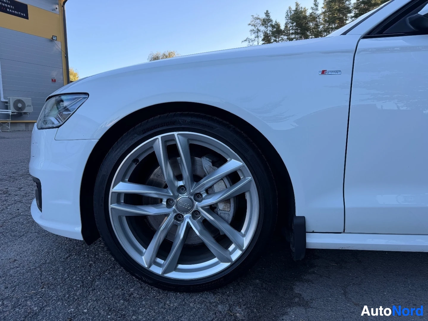 Etuviisto, nokka oikealle: Kuva auton etupyörästä ja etulokasuojasta, jossa on "S line" -merkki. Autossa on hopeanväriset monipuolaiset kevytmetallivanteet ja Bridgestone-renkaat.