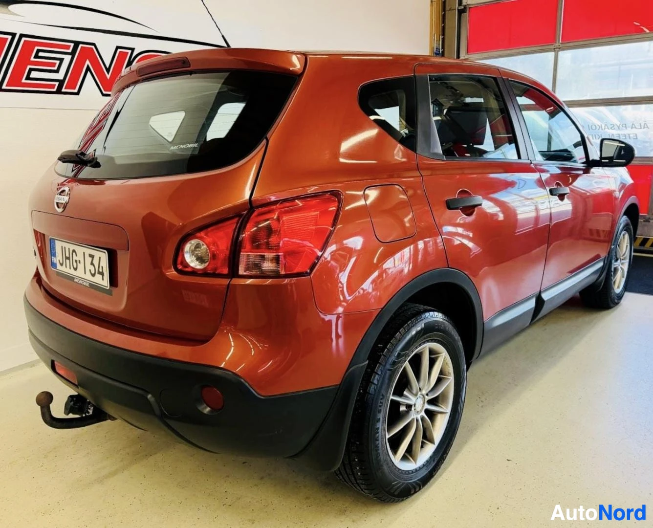 Takaviisto: Oranssi Nissan Qashqai näkyy takakolmanteljanuolelta oikealle, autotallissa. Näkyy takaloukku, takakoneet, takavalot ja vetokoukku.