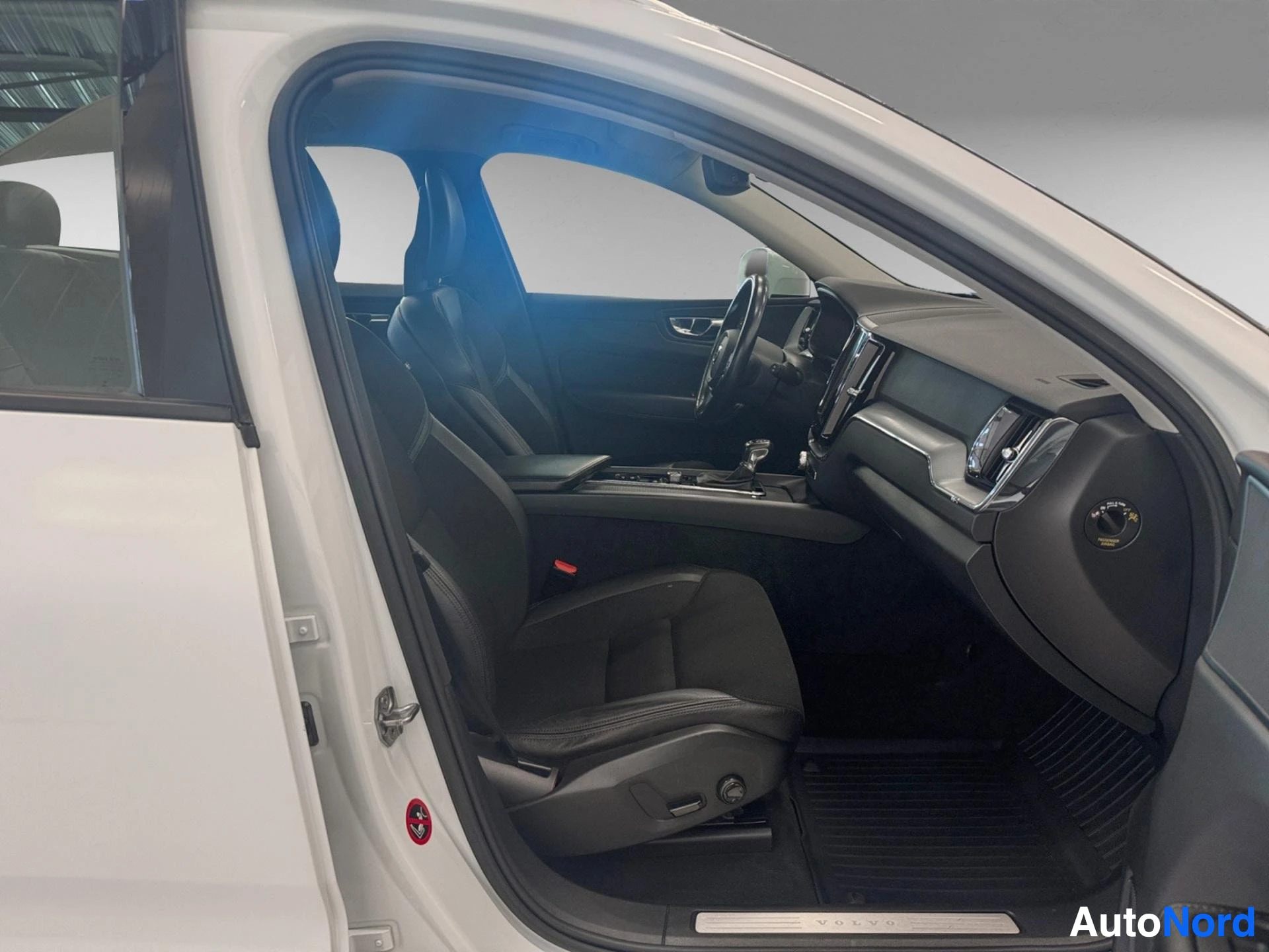 Etuistuimet: Volvo XC60:n avoin kuljettajan ovi näyttää sisätilan sivulta, mustan nahkaisen istuimen, valaistun sisustuksen, näytön ja säätimien näkyvät selvästi.