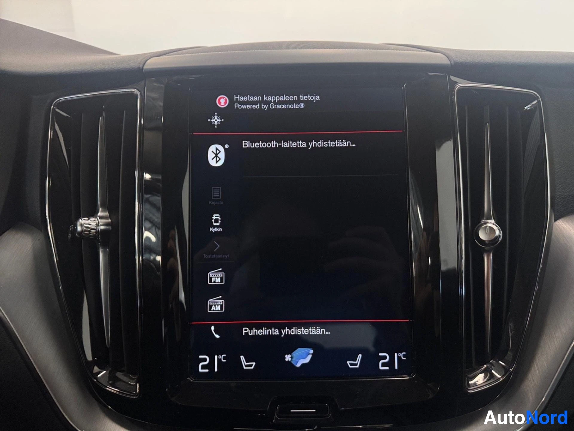 Yksityiskohta: Infotainment-näytöllä näkyy Bluetooth-asetukset ja teksti 'Haetaan kappaleita tietoja'.