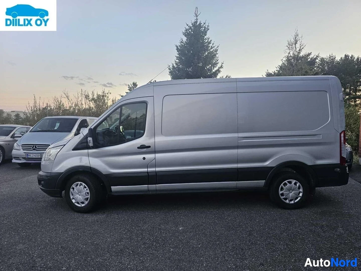 Sivulta: Hopeanharmaa Ford Transit pakettiauto, kuvattu sivusta oikealle päin, varikolla muiden ajoneuvojen rinnalla