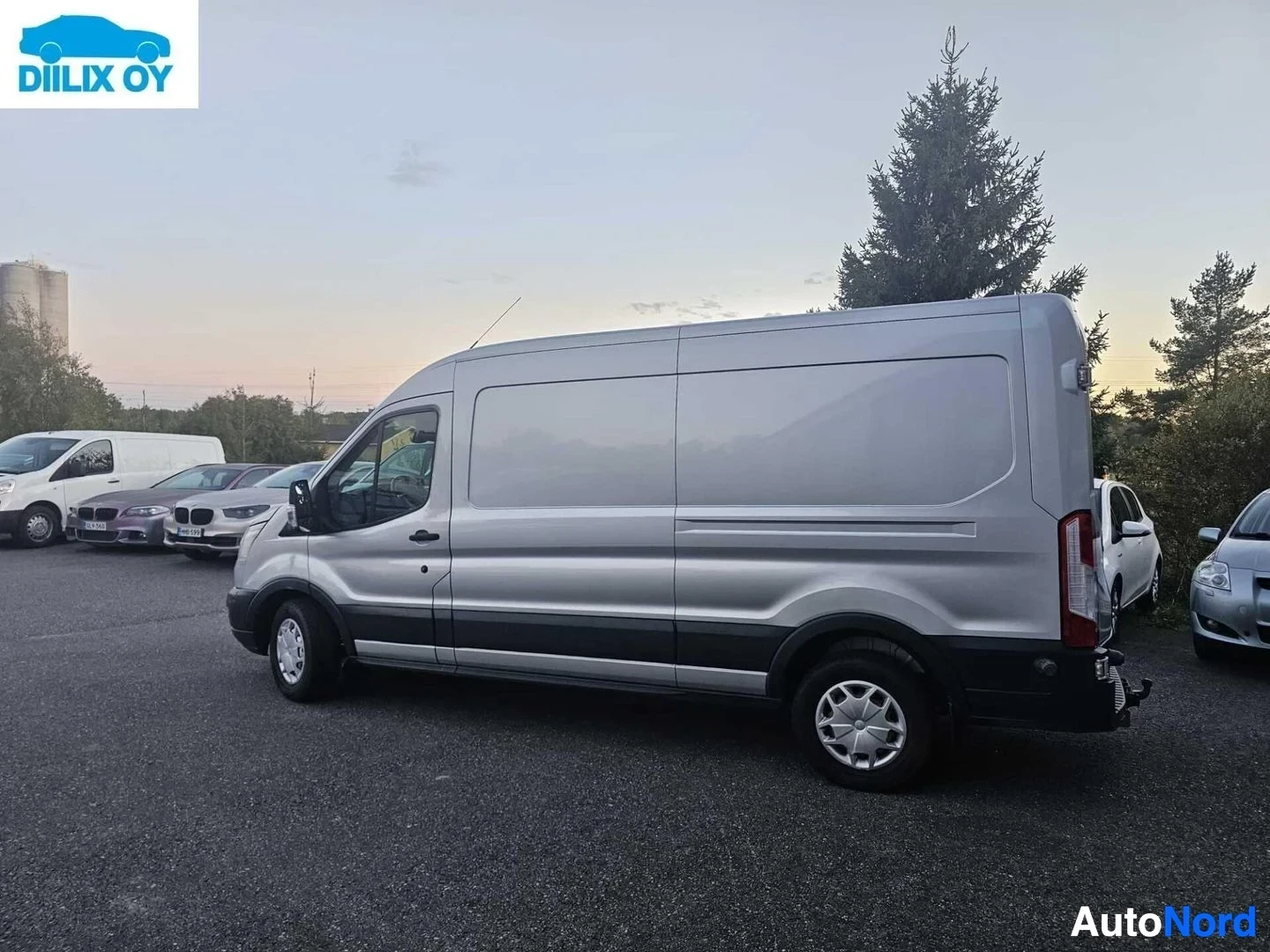 Sivulta: Hopeanharmaa Ford Transit pakettiauto, kuvattu sivusta oikealle päin, varikolla muiden ajoneuvojen vieressä