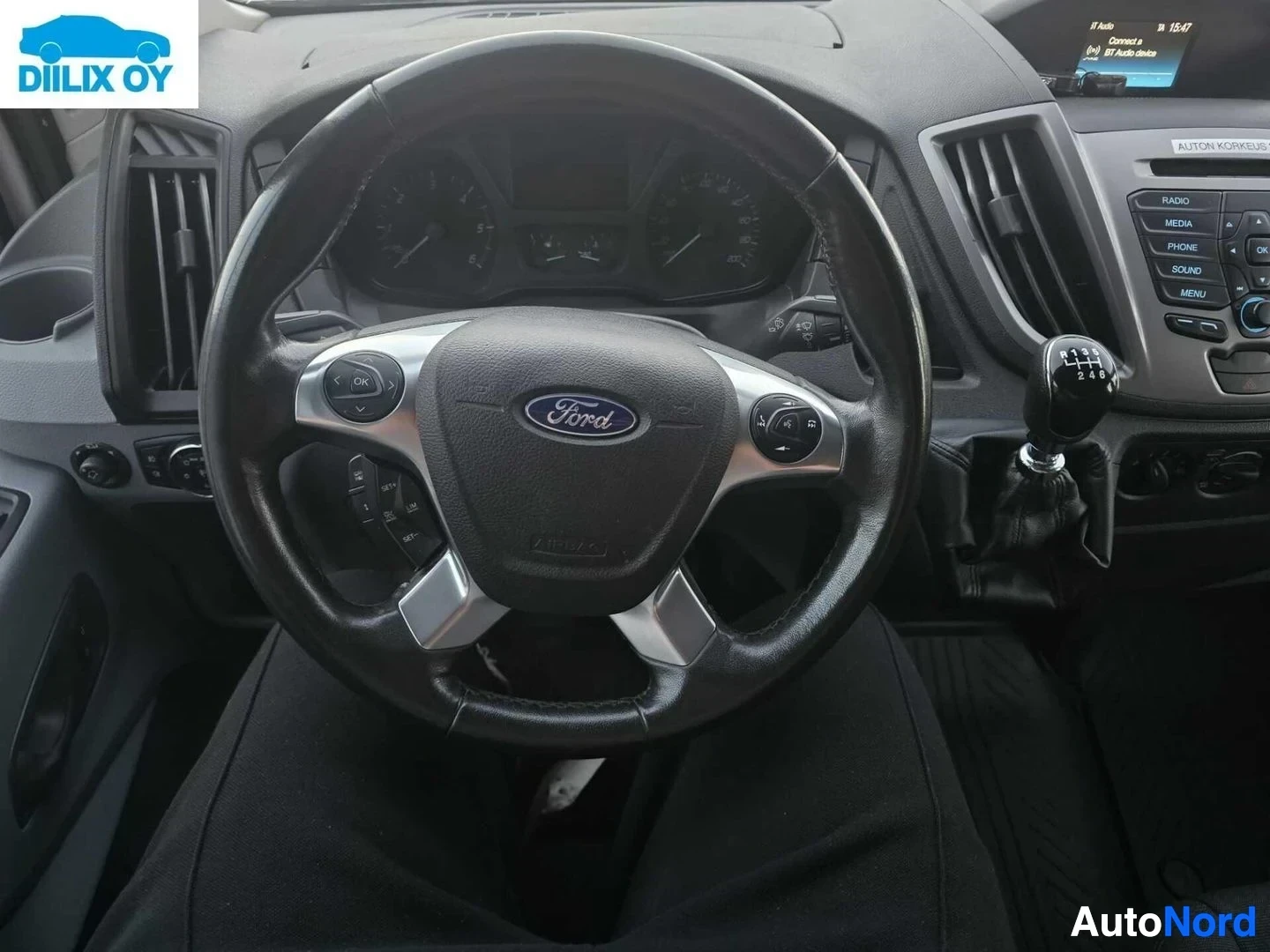Ohjaamo: Ford-ohjauspyörä kuljettajan näkökulmasta, musta nahka ja harmaa kitti, näkyy kojelauta ja ilmastoinnin säätöpainikkeet