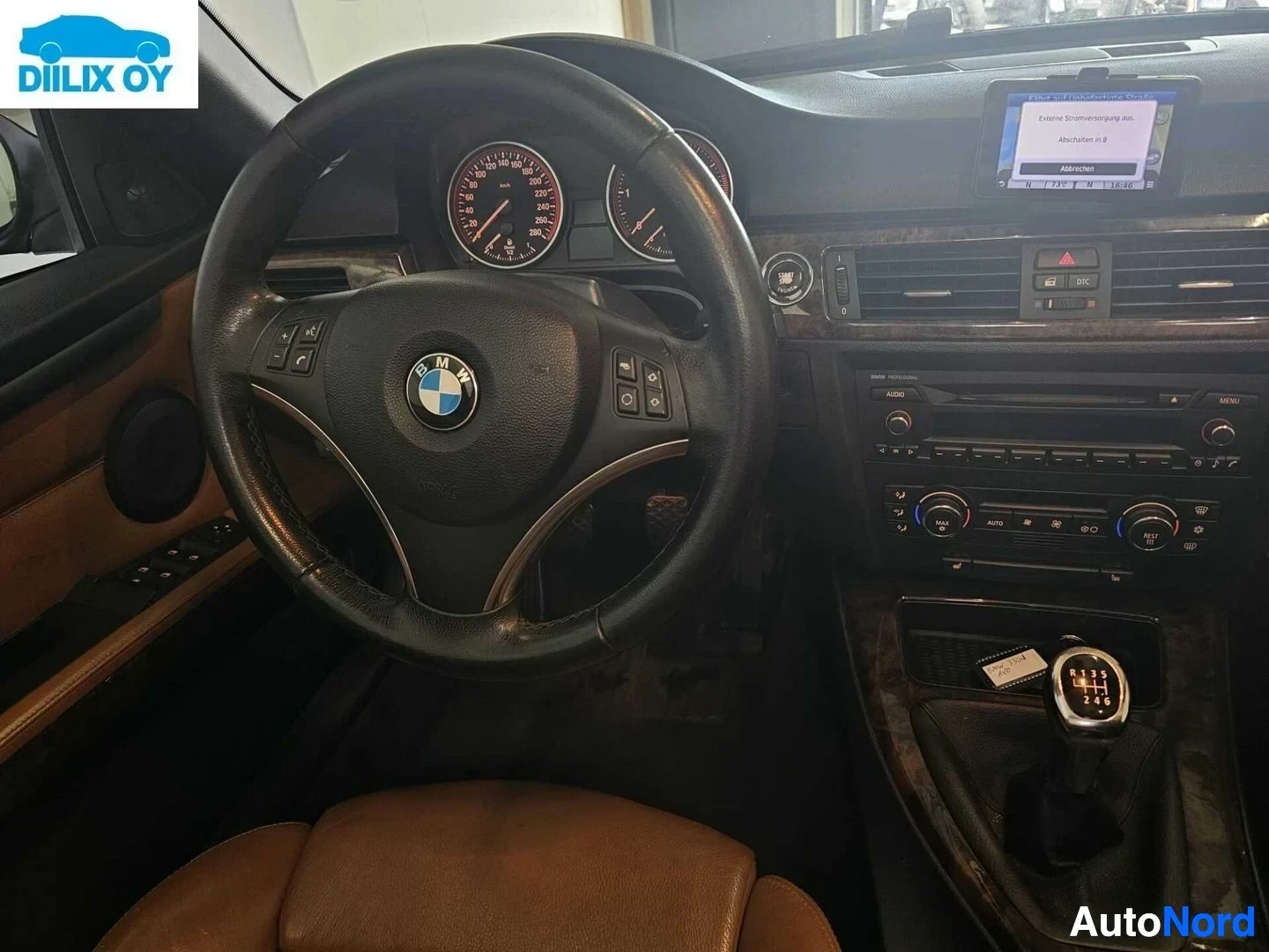 Yksityiskohta: Ohjaamon detaljikuva: ohjauspyörä BMW-logolla, mittaristo punaisilla neuleilla, automaattivaihteisto, ilmastointi-ohjaimet, näyttö kojelaudassa