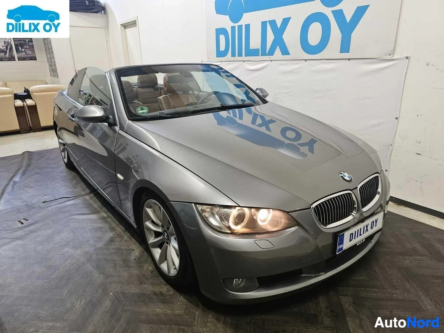Etuviisto, nokka vasemmalle: Hopeanvärinen BMW-avoauto sisätiloissa, etupuoli vasemmalle kääntyneenä, ovi auki.