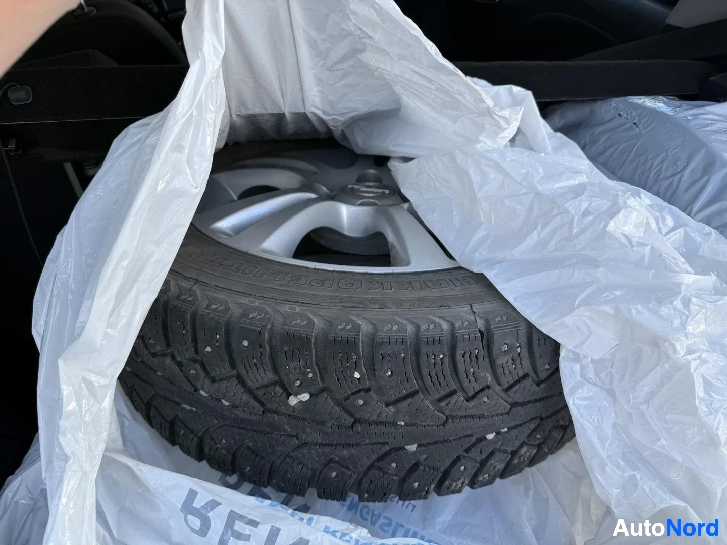 Yksityiskohta: Talvirengas metallivannella, pakkausmateriaaleissa, pinnassa näkyy nastarenkaiden nastoitus ja kuviointi