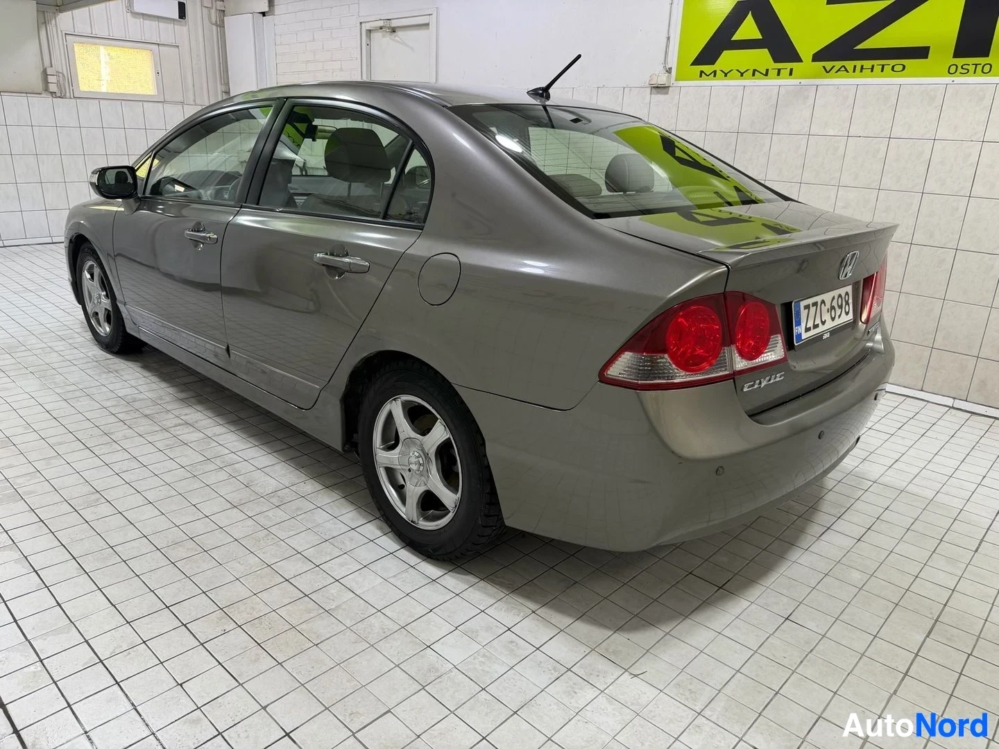 Sivulta: Harmaa Honda Civic neliövetinen profiilinäkymä oikealta, ovi auki. Rekisterilevy näkyvissä. Punaiset takavalot, valkoiset metalliseokset