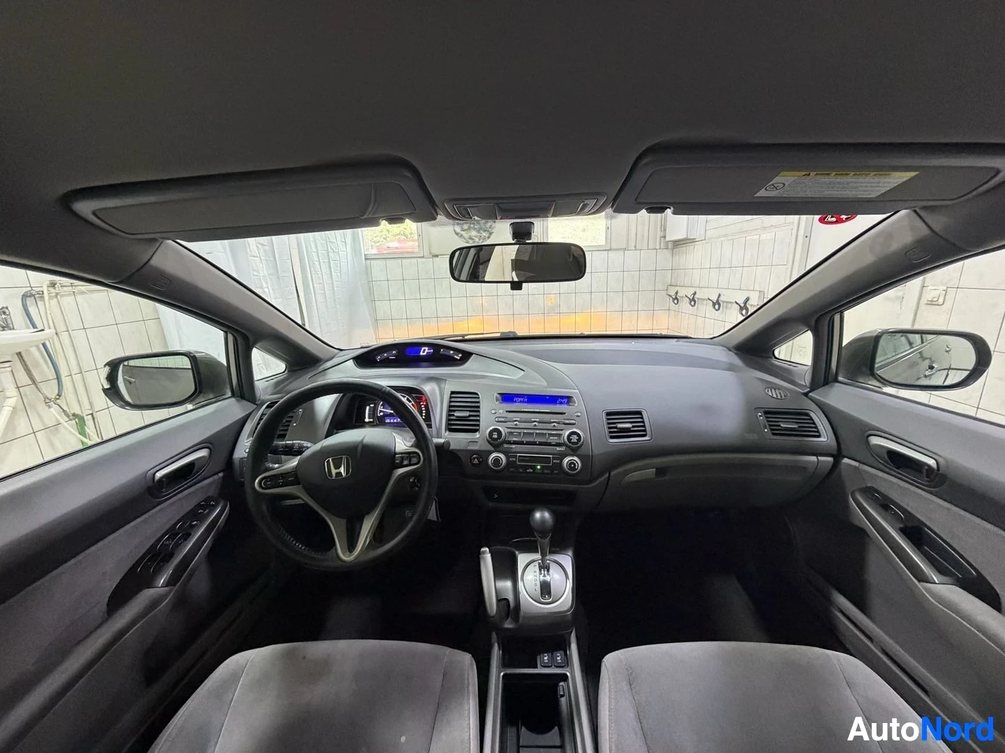 Ohjaamo: Honda-merkkinen sedan sisäkuva, ratti, ohjauspyörällä kuvio, kojelauta sinisellä näytöllä, harmaat istuimet, panoraaminen katto, säädettävät käsinojat vasemmall
