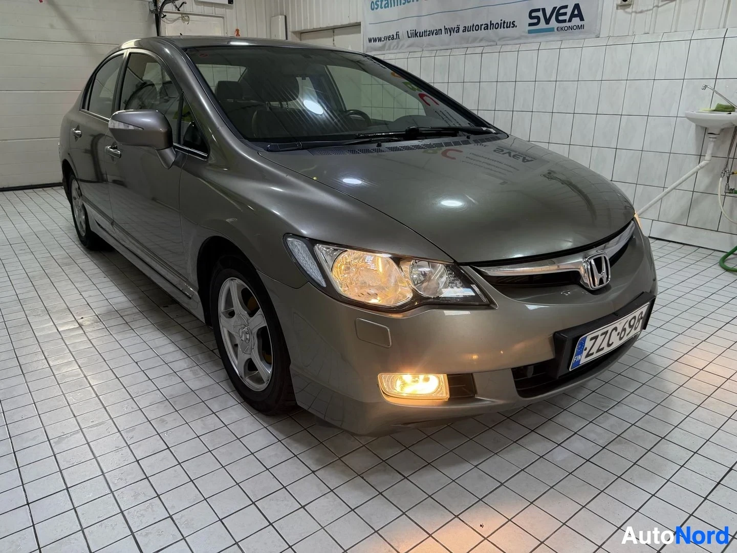 Etuviisto, nokka oikealle: Kokonainen Honda Civic 4D sedan etupuolelta vasemmalle katsottuna. Harmaa metallinen ajoneuvo, LED-päivänvalot, varsi- ja takavalojen sähköä syöttävä yks