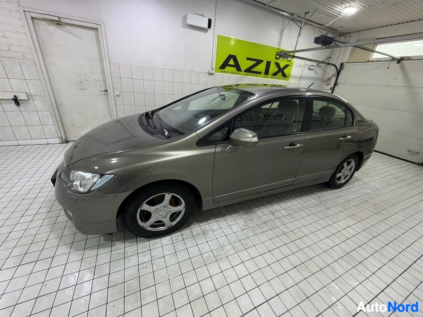 Sivulta: Harmaa Honda Civic neliövetinen vasemmalta katsottuna, hallissa. Valkoiset metalliseokset, pysäköity halliin.