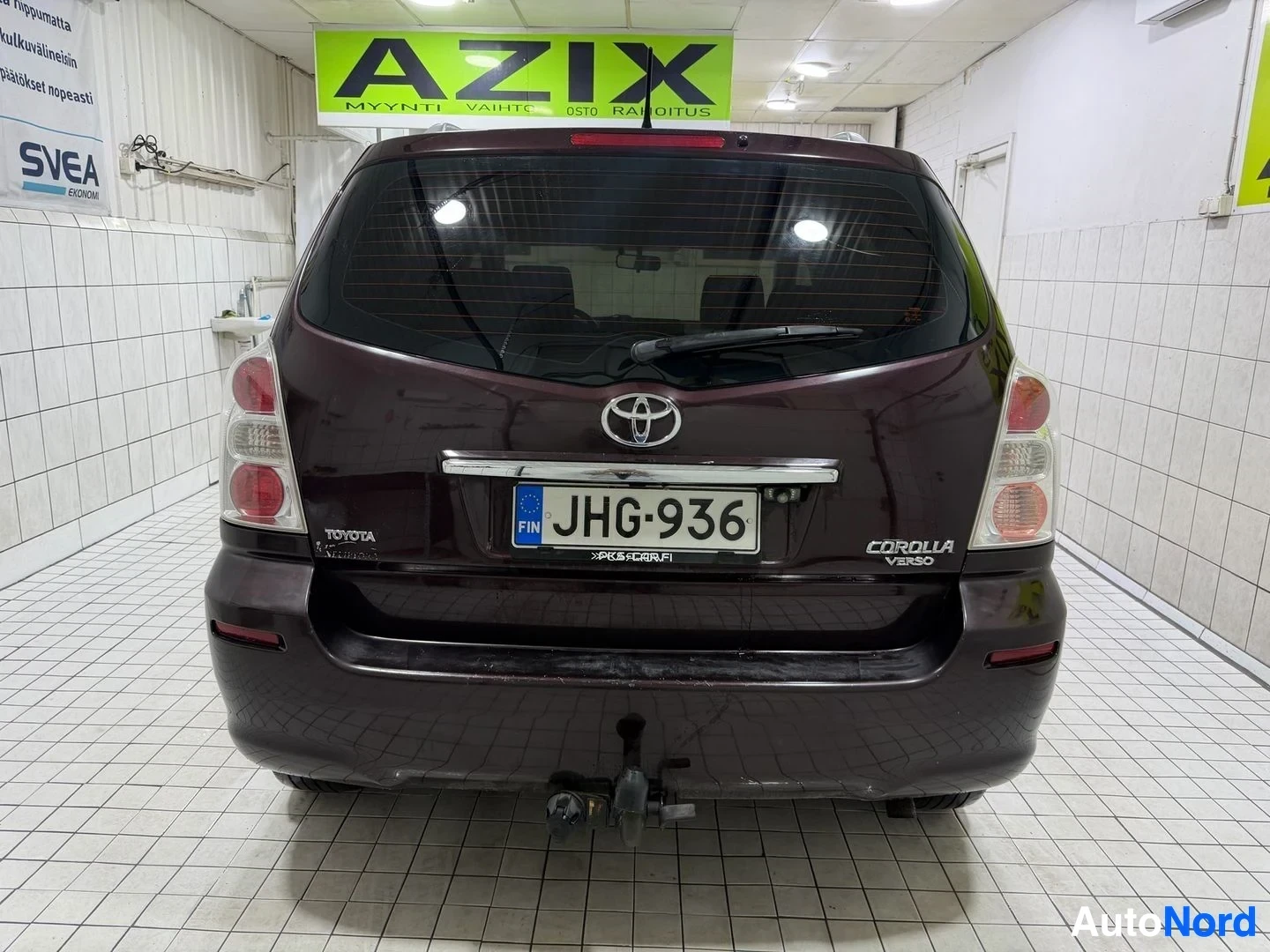 Takaa: Tummanruskea Toyota Corolla Verso takaosa, rekisterikilvessä, näkyy Toyota ja Corolla Verso merkit takakannessa, vetokoukku näkyvissä