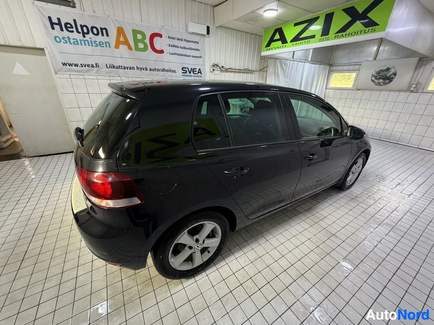 Sivulta: Volkswagen Golf sivulta oikealta, musta auto, sisätiloissa, valkoisia vanteet näkyvissä
