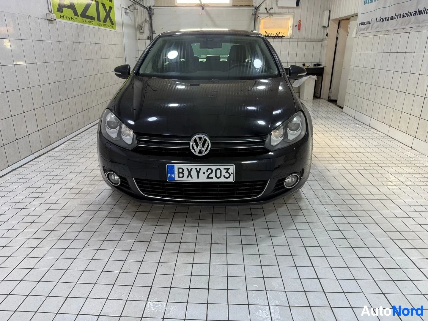 Edestä: Musta Volkswagen Golf etuviistosta suoraan edestä, sisätiloissa, rekisterikilpi, sumuvalaisimet näkyvissä
