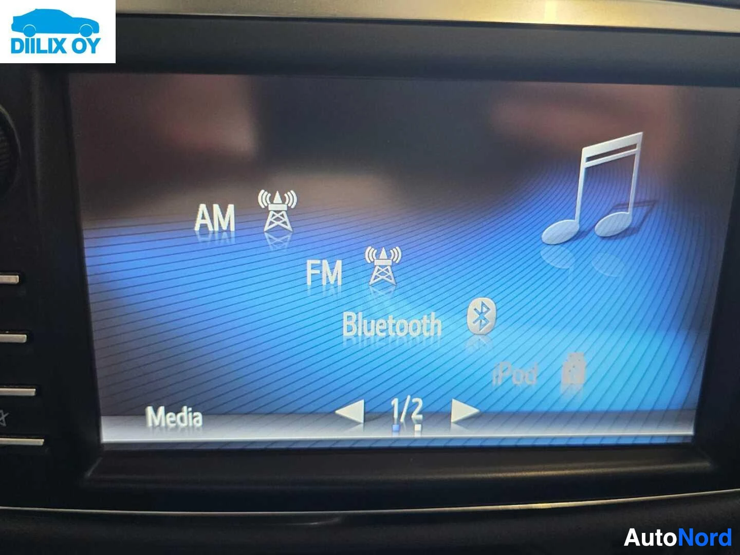 Yksityiskohta: Auton infotainmentin näyttö, jolla näkyy Media-valikko. Valikossa AM ja FM radiolähetykset, Bluetooth-yhteys ja iPod-vaihtoehto sekä musiikkisymboli. Näytön ala