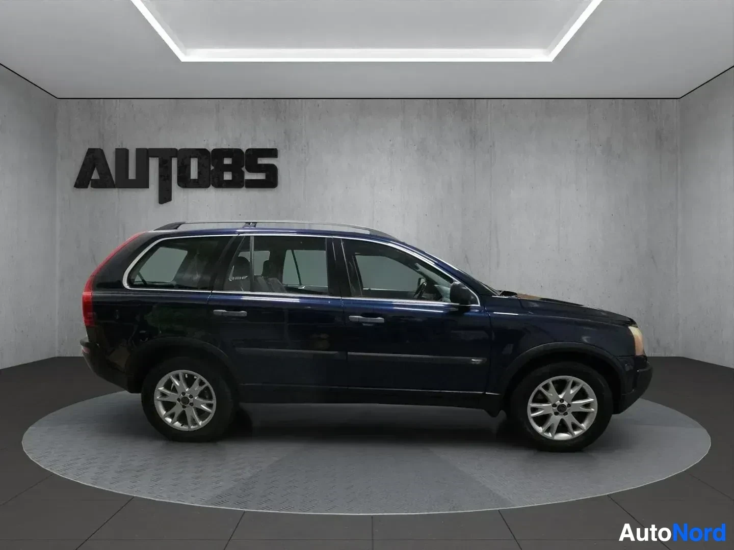 Sivulta: Siniset Volvo XC90:n sivukuva valaistussa studiossa. Auton katolla on kattotelineet.