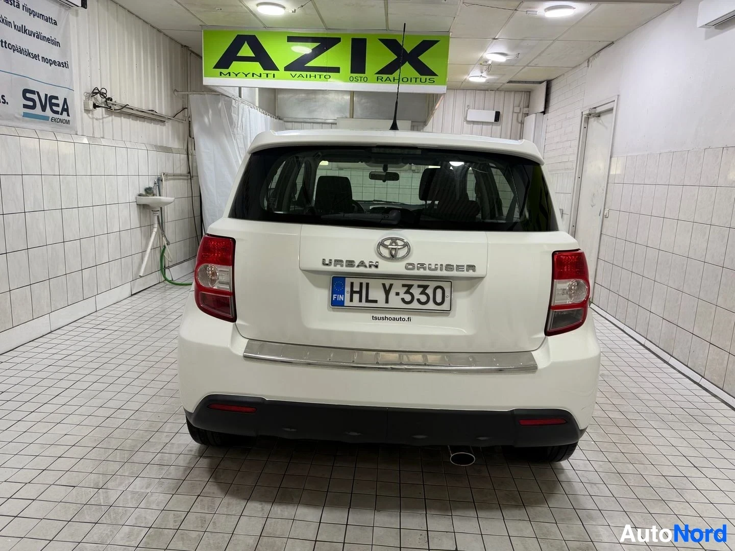 Takaa: Valkoinen Toyota Urban Cruiser, takapuoli hallissa, takaosan merkinnimi 'URBAN CRUISER' näkyy selvästi.