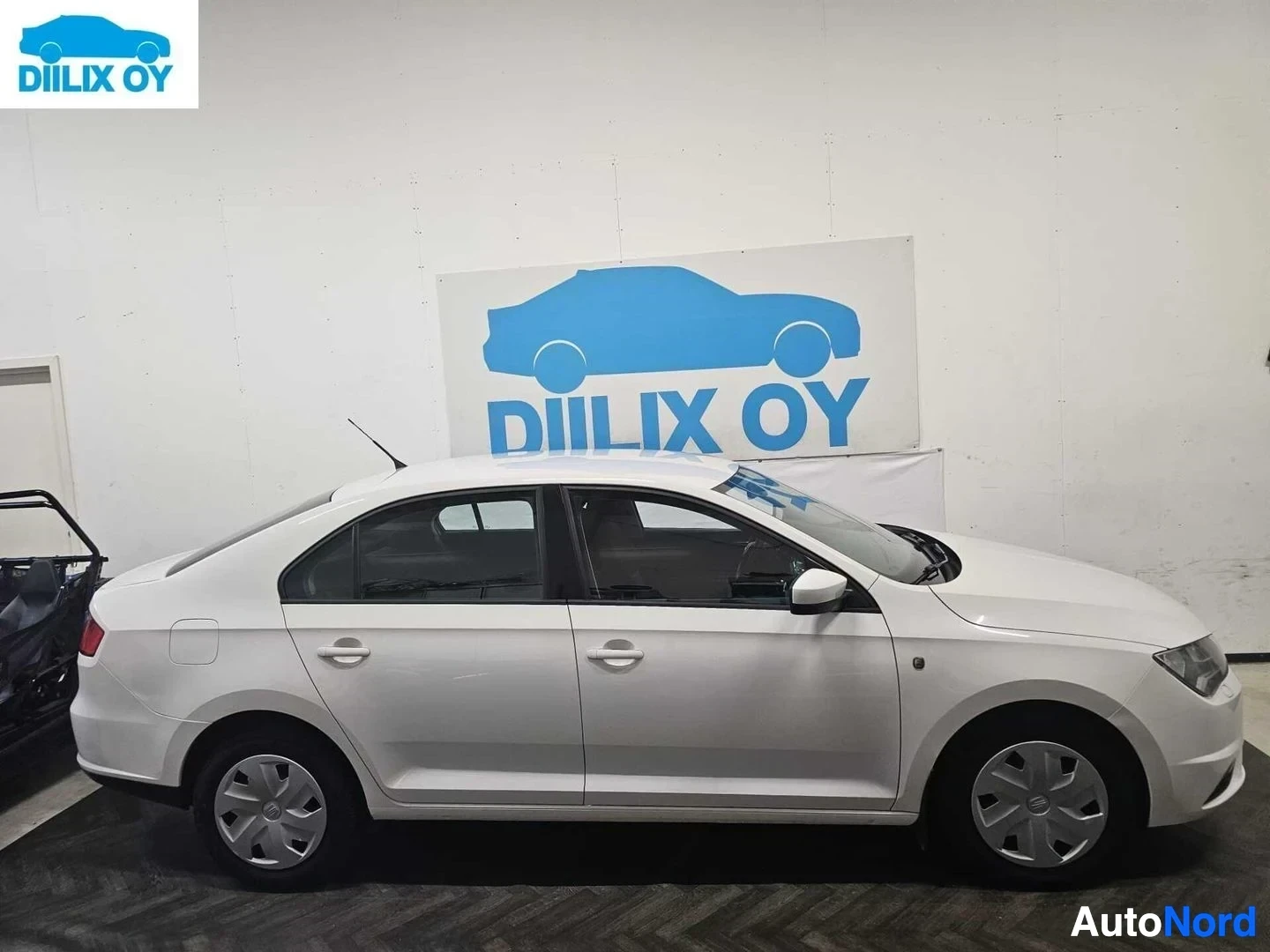 Sivulta: Valkoinen Seat Toledo seisoo autotallissa sivusta katsottuna, oikea sivu näkyvissä. Rekisterikilvessä näkyy teksti